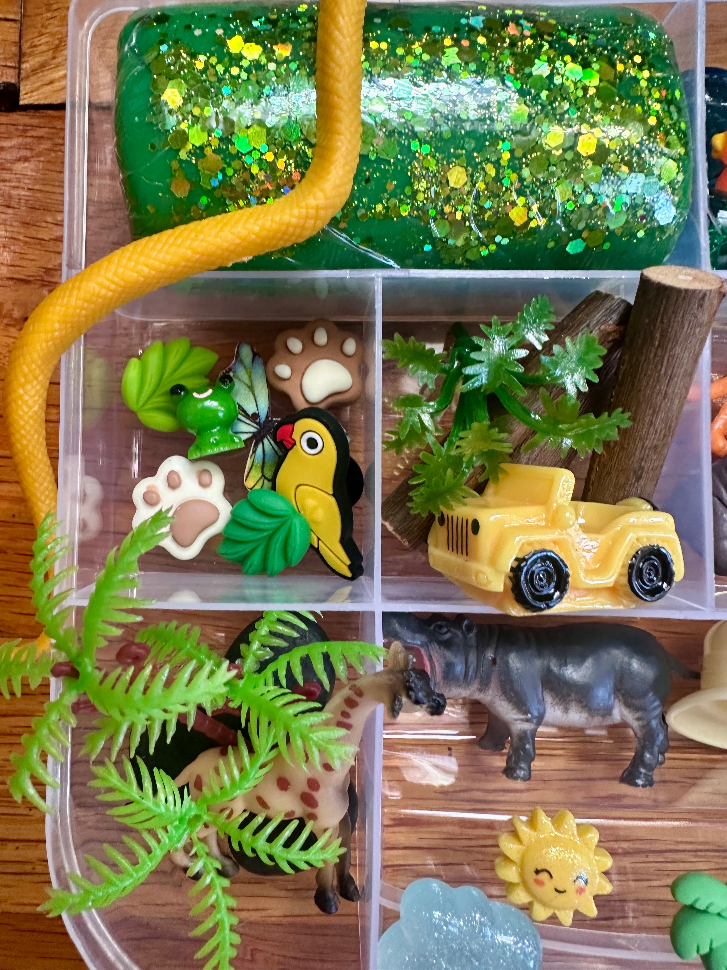 Toy set with animals, plants, and a car in a clear plastic container on a wooden surface.